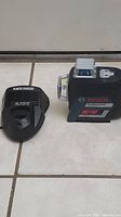 Laser level and battery charger seen from the side on tiled floor; charger labelled AL 1110 CV.
