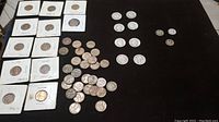 Wide shot of all coins laid out including silver quarters, Mercury dimes, and wheat pennies in protective holders and loose on a black surface