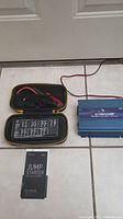 Both the Samplex PST-15S-12A sine wave inverter and DBPOWER jump starter portable charger with cables and manual on tile floor.