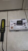 Garrett Super Scanner V metal detector next to Bunker Hill Security Color Security System box on tile floor.