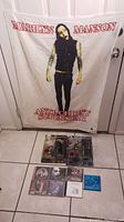 Full view of Marilyn Manson fabric banner with two collectible figures and seven CDs arranged on the floor in front of it.