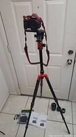 Red Nikon D5300 camera mounted on orange and black Zomei tripod with two lenses and manuals arranged on floor