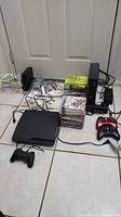 Wide view showing three consoles, controllers, stacks of game cases
