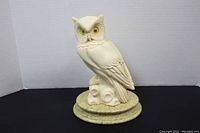 Full view of white alabaster horned owl figurine on a circular textured stand, facing left.