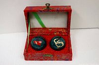Pair of Baoding health balls inside their decorative red fabric-covered case, showing the dragon and gold symbol designs on each ball.