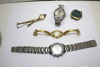 Overview of the five watches laid out on white background showing three men's watches at top with silver and gold tones, and two women's watches at bottom including one with broken band.