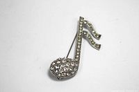 Close-up photo of the musical note rhinestone brooch on a white background showing full view of stones and brooch details.