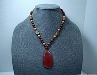 Full view of the 18-inch long necklace with deep pinkish-red art glass pendant on display bust.