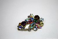 Brooch showing multicolored navette and round rhinestones with iridescent shine.