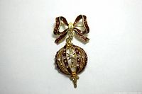 Front view of the gold-tone Christmas brooch with red enameled ribbon and dangling bulb ornament decorated with rhinestones and stars.