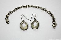 Full view of sterling silver bracelet and pair of earrings on white background.