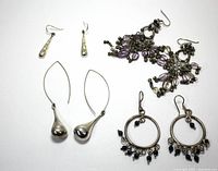 Four pairs of sterling silver earrings arranged on white background: chandelier with purple and black beads, circle hoops with black beads, large teardrop dangles, and long teardrop dangles.