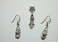 Sterling silver pendant and matching earrings with amethyst stones and Irish knot design on white background.