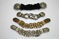 Set of four sweater clips laid out showing variety of metal chain and clip designs including black elastic band and decorative round clips.