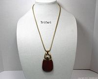 Full view of the vintage Crown Trifari necklace on display bust showing the gold-tone chain and large red lucite pendant.