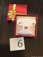 Pair of 14KT white gold peridot stud earrings displayed in a red gift box with gold bow.
