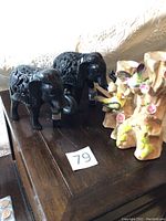 Two black resin elephants on wooden surface with intricate carved details and removable trunks, positioned near two ceramic vases shaped like tree stumps with painted birds and flowers.