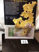 Photo shows entire collectible card featuring a 0.10 gram 24 karat gold ingot in a protective sleeve with gold nugget artwork and text explaining purity and anti-counterfeiting features.