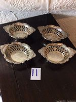 Set of four Birks sterling silver lace cut dishes shown from above on black surface.