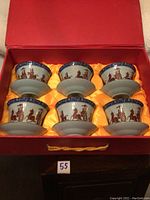 Box containing six porcelain tea cups with lids and saucers, neatly arranged on yellow satin lining inside a red box.