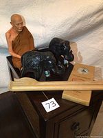 Overall lot showing Buddha figurine sitting on a dark wooden cabinet with two black carved elephants, a box of natural candles, and wooden back scratchers in front.