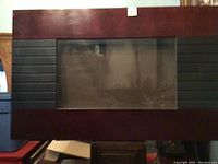Front view of electric fireplace showing wood frame, glass front, and black vertical vent slats on the side.