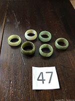 Six jade rings arranged on dark wooden surface showing varied green hues and sizes.