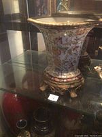 Side view of the large flared porcelain vase with floral design on bronze base inside a glass display case.