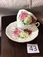 Front angle of Queen Anne floral teacup stacked on matching saucer showing pink and yellow rose designs and gold rim.