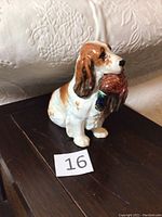 Front and side views of the Royal Doulton Cocker Spaniel ceramic figurine holding a pheasant in its mouth, placed on a dark wooden surface with embroidered white fabric in the background.