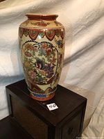 Full view of ceramic Satsuma vase with visible birds and floral artwork standing on wooden cabinet.
