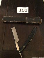 Photo showing vintage straight razor with black handle and original black storage box on a wooden surface.