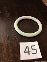 Top-down view of jade bangle on dark wood surface with lot number card visible