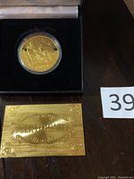 Gold plated coin in clear round capsule on black velvet background alongside gold ornate certificate card with the word CERTIFICATE