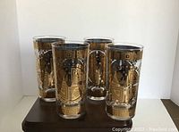 Four vintage Culver highball glasses featuring heavy gold accents and clear glass, displayed on wood surface.