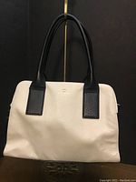 Front view of the white pebbled leather purse with black handles and minimal gold Kate Spade logo at center.