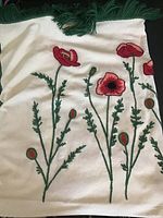 Cream blanket with green fringe and detailed needlepoint red and pink poppy flowers with green stems and leaves shown spread out.