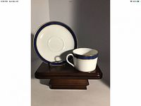 Porcelain cup and saucer with blue and gold band displayed on wooden stand.