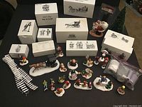 Wide view of all figures with their original boxes in the background. Shows figures including Santa with children, horse carriage, Christmas tree, and many small figurines on snow bases.