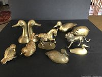 Overview of all brass items on display, showing ducks, horse, lion, pig bank, and smaller bird figurines on black background.