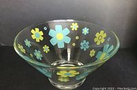Clear glass serving bowl with blue and green stylized flowers decorating the exterior, photographed under natural light on a dark background.