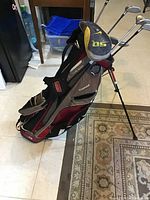 Angular side view of Sun Mountain Three 5 golf bag in red/gray showing stand, straps, and some clubs inside.
