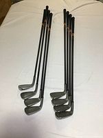 Photo showing full set of golf irons laid out in two rows on a white surface. Includes eight clubs, 3 through 9 irons plus pitching wedge, all right handed with black shafts and grips.