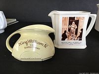 Two whisky jugs side by side, showing the King William IV jug in light yellow and the Bell's jug in white with a label image