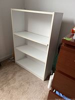 White bookcase shown from left angle in carpeted room beside dark wood dresser.