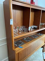 Three-quarter view of wooden buffet hutch showing top and base with three compartments, sliding glass doors, glass shelves and decorative tile insets