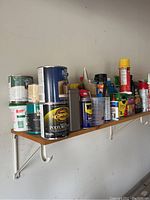 Shelf with assorted paint cans, spray cans, and bottles including Rust-Oleum and Cabot brands.