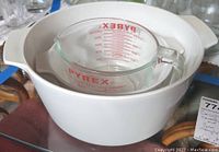 White Corning Ware casserole dish with matching lid holding a Pyrex 4-cup measuring cup.