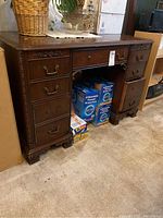 Front view of vintage wooden desk with brass hardware and carvings, drawers intact; shows overall condition and style.