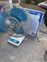 Photo shows vintage-style table fan with blue blades, metal grille with rust, white base with control switches and power cord, alongside box fan original box.